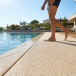 Pieds nus marchant sur un revêtement antidérapant clair au bord d'une piscine moderne sous le soleil éclatant.